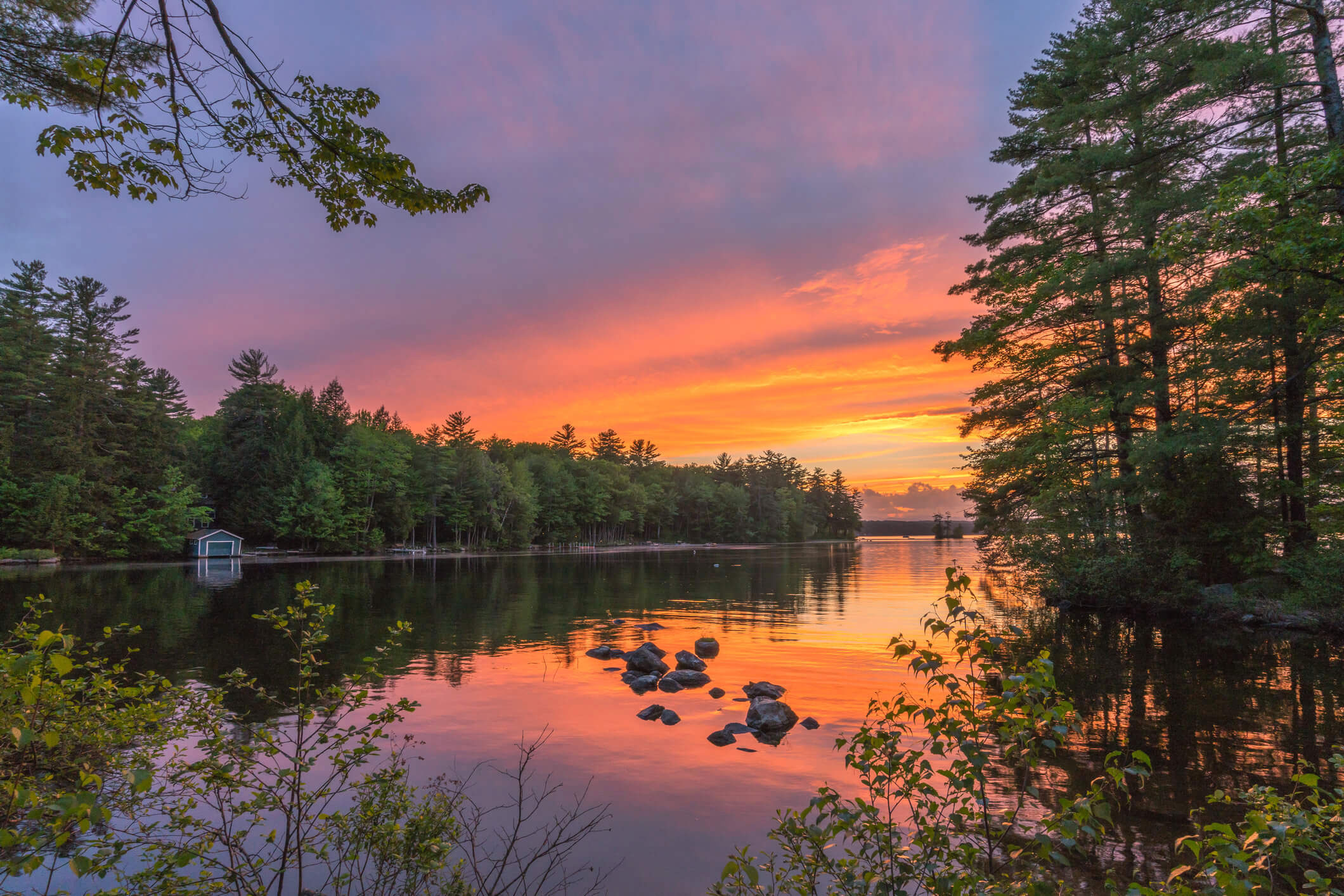 The image depicts a serene sunset over a lake with trees and a dock visible, set against a clear sky.