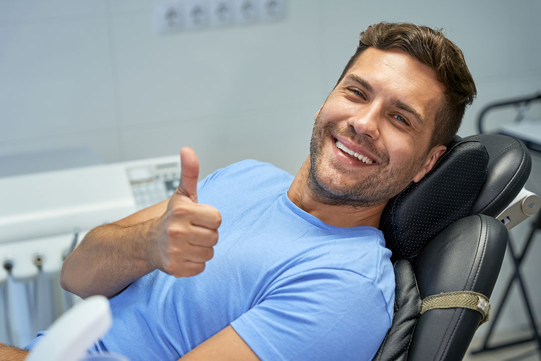 The image shows a man sitting on a chiropractic table with his thumbs up, smiling at the camera.