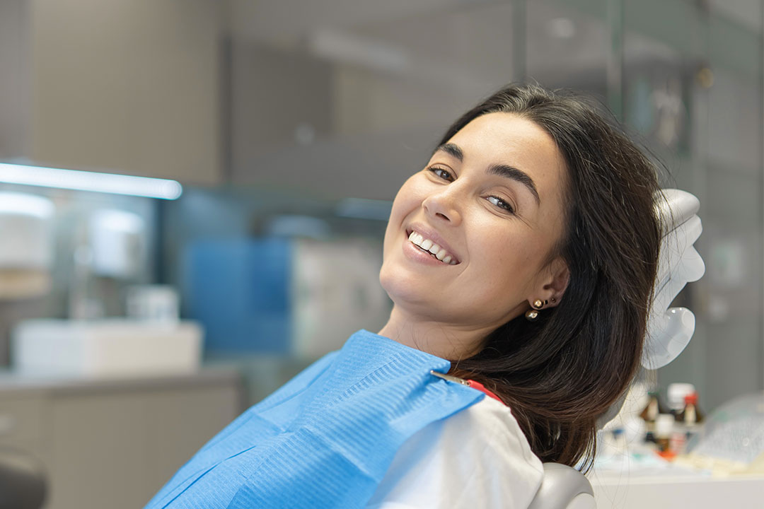 A woman wearing a white dental gown and smiling at the camera while sitting in a dentist s chair.