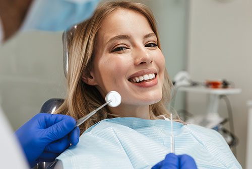 A woman sitting in a dental chair with a smile, receiving dental care from a dentist who is adjusting her braces while wearing protective gloves.