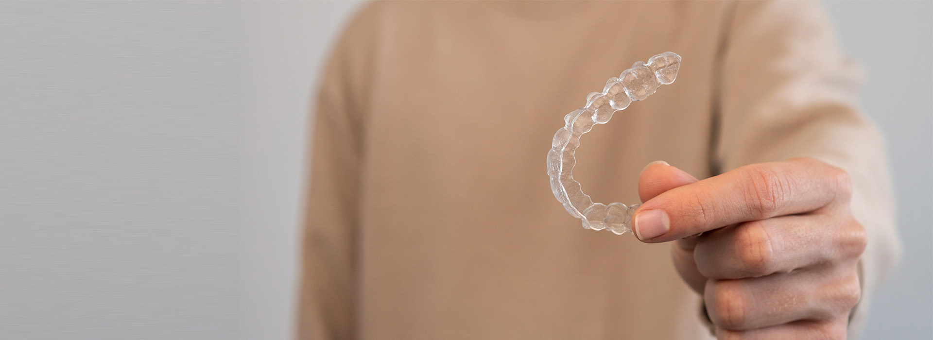 A person s hand holding a transparent plastic ring against a blurred background.