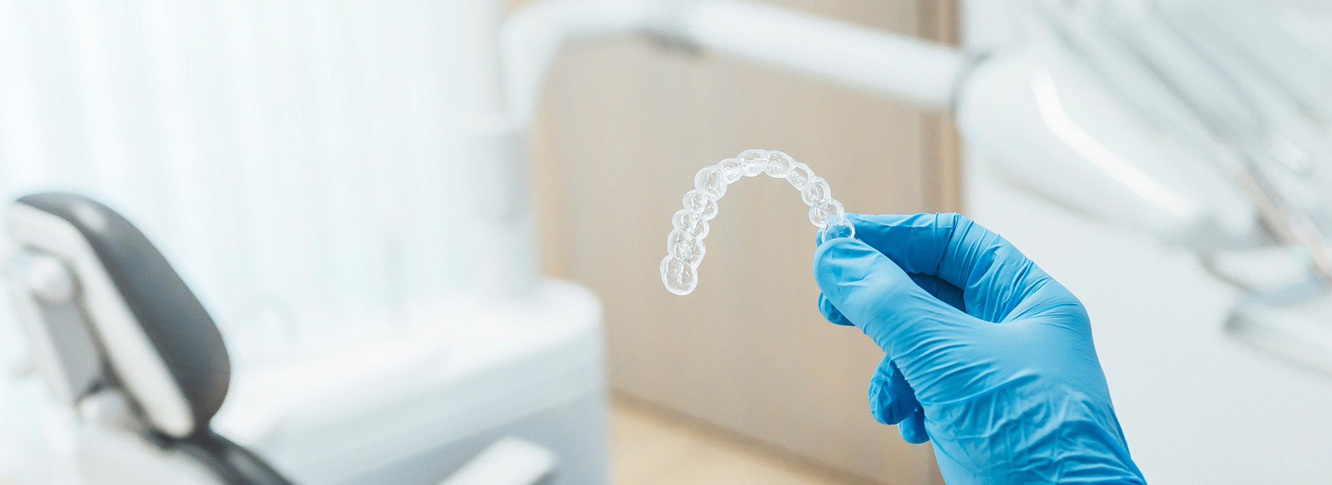 A hand holding a transparent object against a blurred background with medical equipment visible.