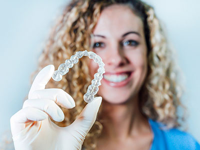 A woman holding up a clear plastic bracelet on her finger with a smile.