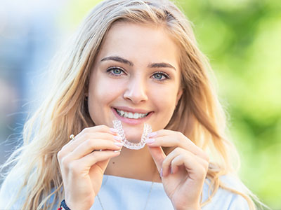 The image shows a young woman holding a toothbrush with a smile on her face.
