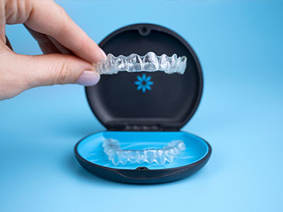 The image shows a hand holding an open dental impression tray with a clear imprint of teeth inside, placed next to a closed, black box containing another set of teeth-shaped molds.