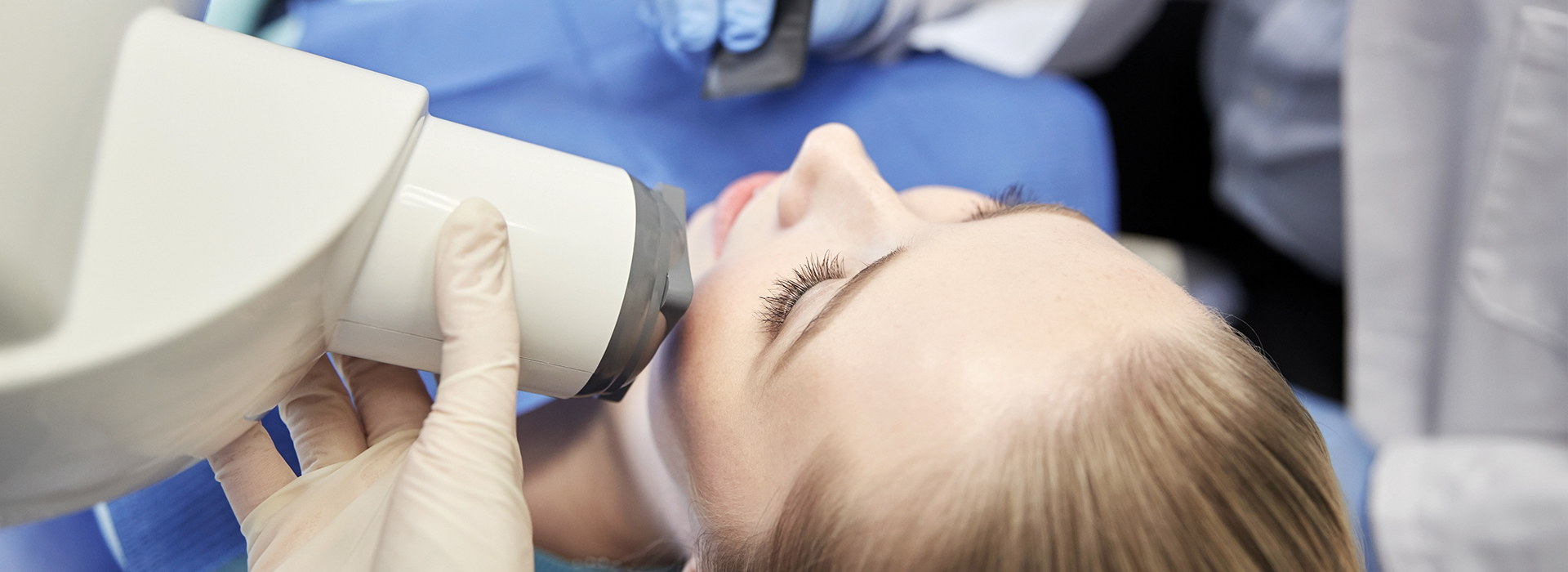 A person receiving dental treatment with a specialized device, possibly a microscope or camera, focused on their mouth.