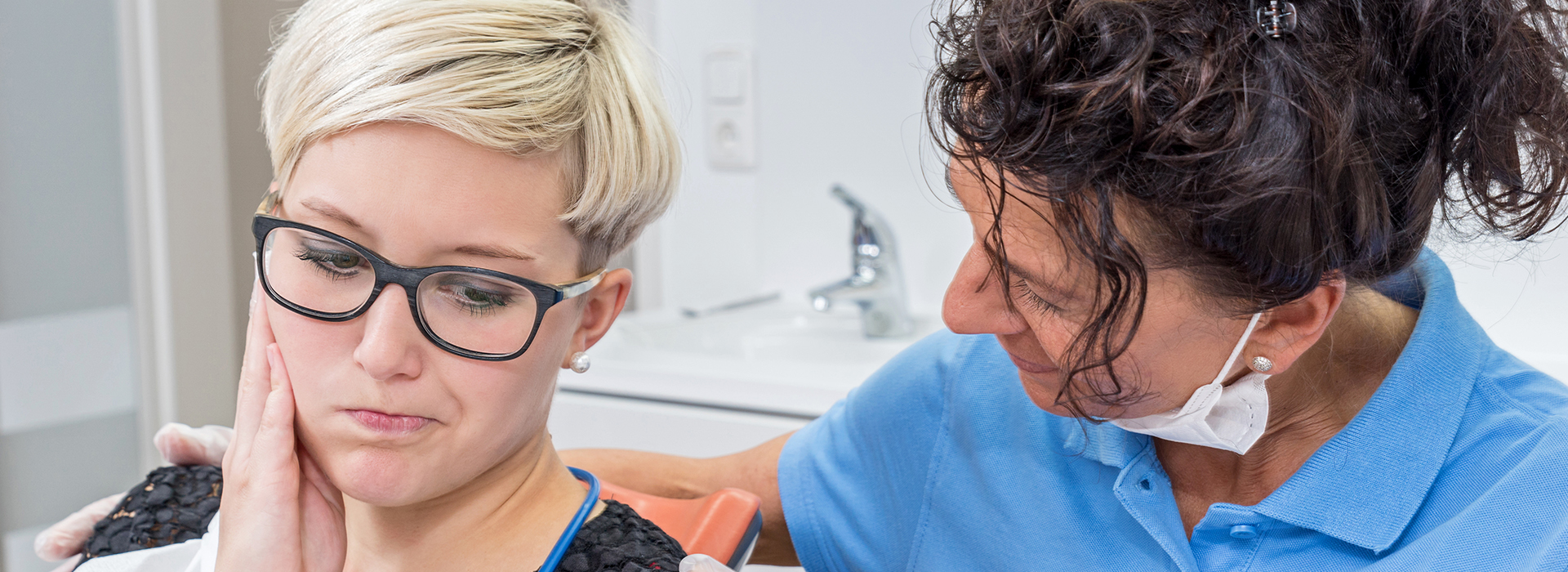 A dental hygienist assisting a patient with dental care while wearing protective eyewear.