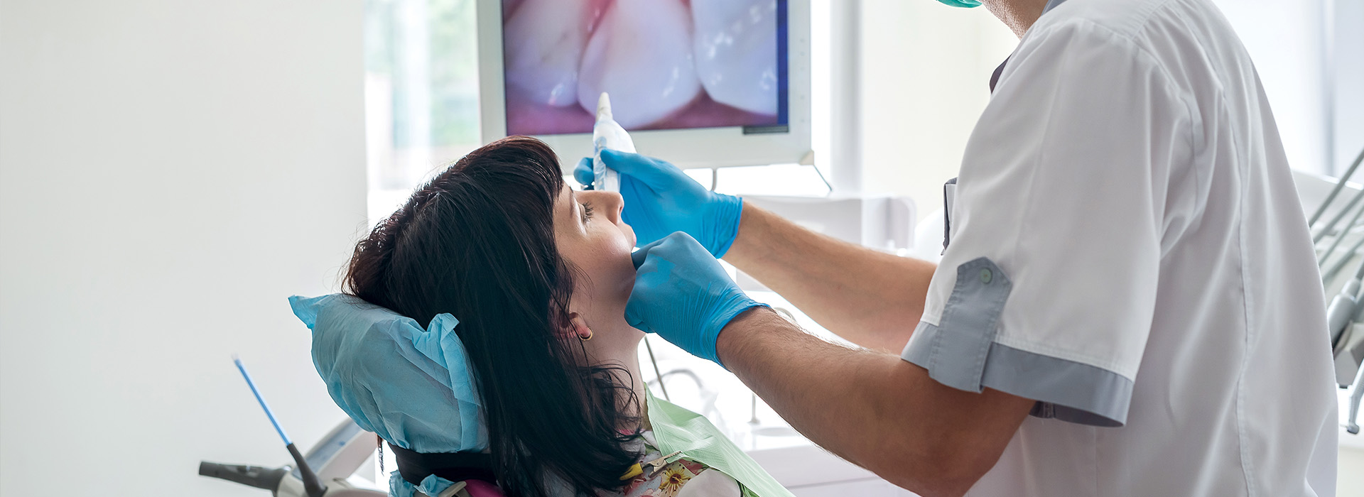 The image shows a dental professional performing a procedure on a patient s mouth using dental tools and equipment, with the focus on the interaction between the two.