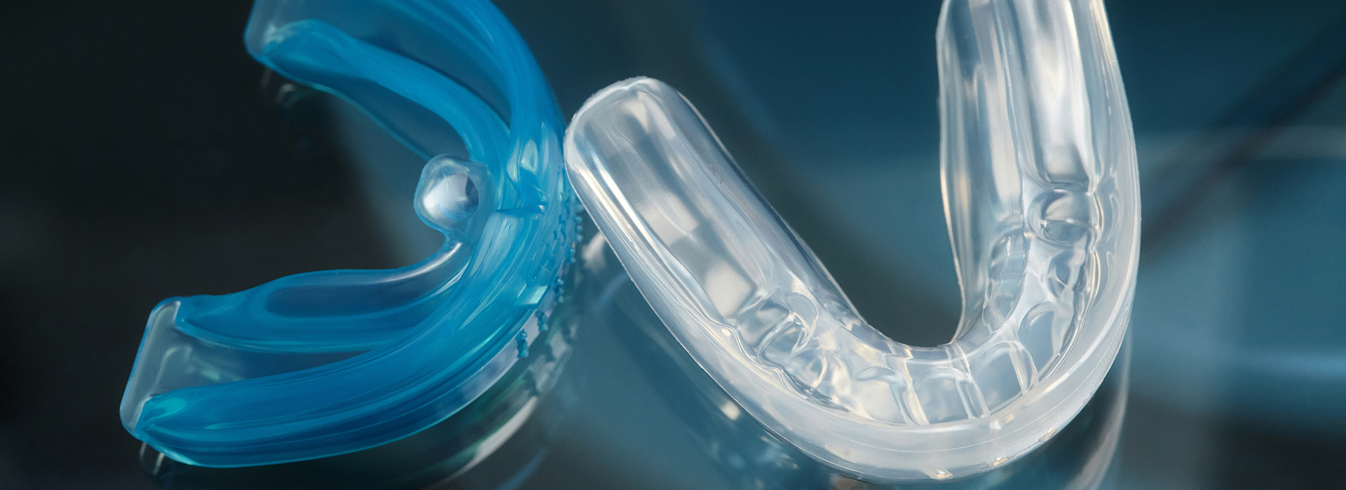 The image shows a close-up of a blue toothbrush with clear bristles against a blurred background, likely meant for dental hygiene use.