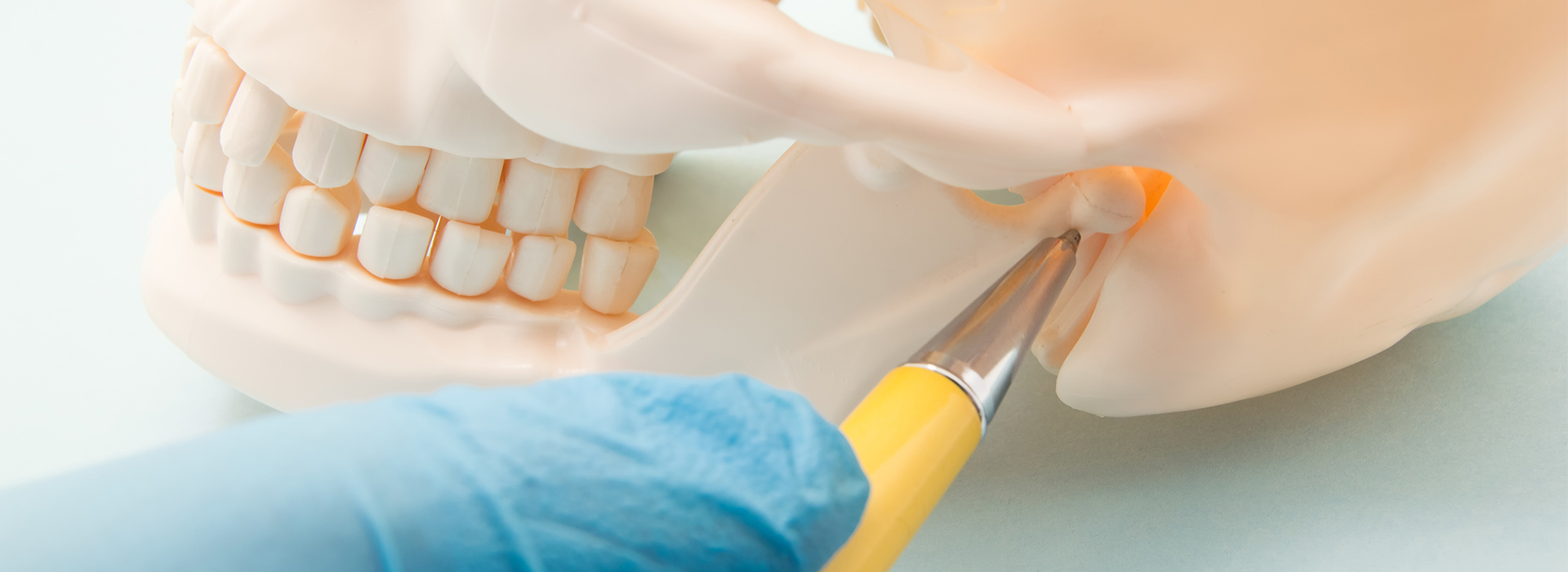 A close-up photograph of a dental implant being placed into a model mouth by a dentist s hand, with a blue surgical glove and a yellow instrument visible.