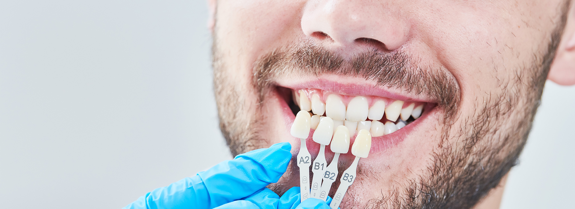 The image features a person smiling at the camera with their teeth, holding a toothbrush near their mouth, and wearing a blue surgical mask.
