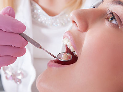 The image shows a person receiving dental treatment with a dentist performing the procedure, using a dental mirror to examine their mouth.