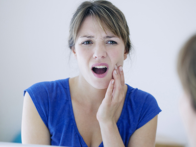 The image shows a woman with her mouth open, expressing surprise or shock, while looking in a mirror at her own face.