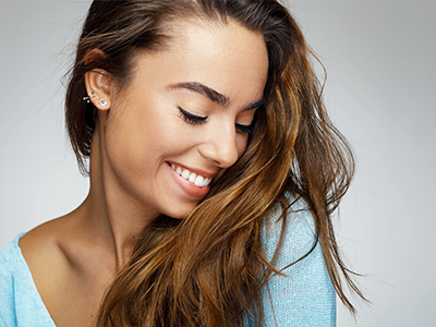 This image features a young woman with long hair smiling at the camera. The background is plain and does not provide any additional context or information about the setting.