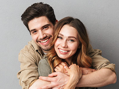 An adult couple embracing each other with smiles, posing against a light background.