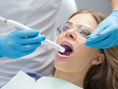 The image shows a dental professional performing an oral examination on a patient using a digital device for visualization, with the patient s mouth open wide for the procedure.