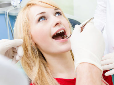 The image shows a woman undergoing dental treatment, with a dentist performing a procedure on her teeth while she is seated in a dental chair.