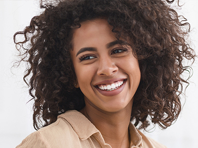 A smiling woman with curly hair, wearing a light-colored top, against a white background.